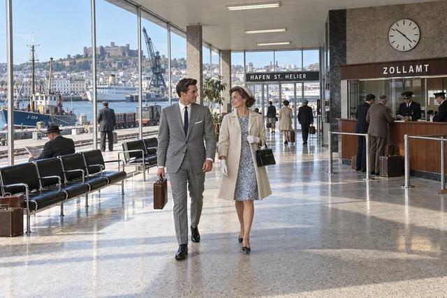 Fictional 1964 colour interior of St Helier's glass-fronted Customs terminal, with a well-dressed couple walking past seating, officials and harbour windows.