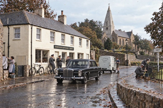 Fictional 1964 colour photograph below Trinity Church, showing the former British Hotel marked Kameradschaftshaus Trinity, SS men, a black Mercedes, local activity and the church spire.